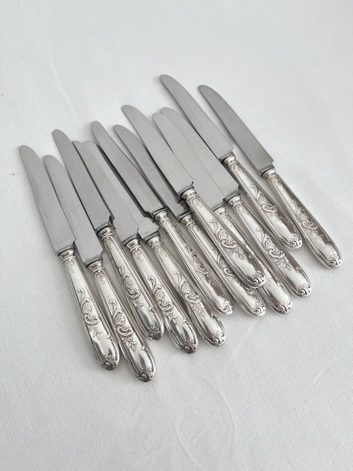 12 antique silver-plated knives with acanthus shell decoration and stainless steel blades.