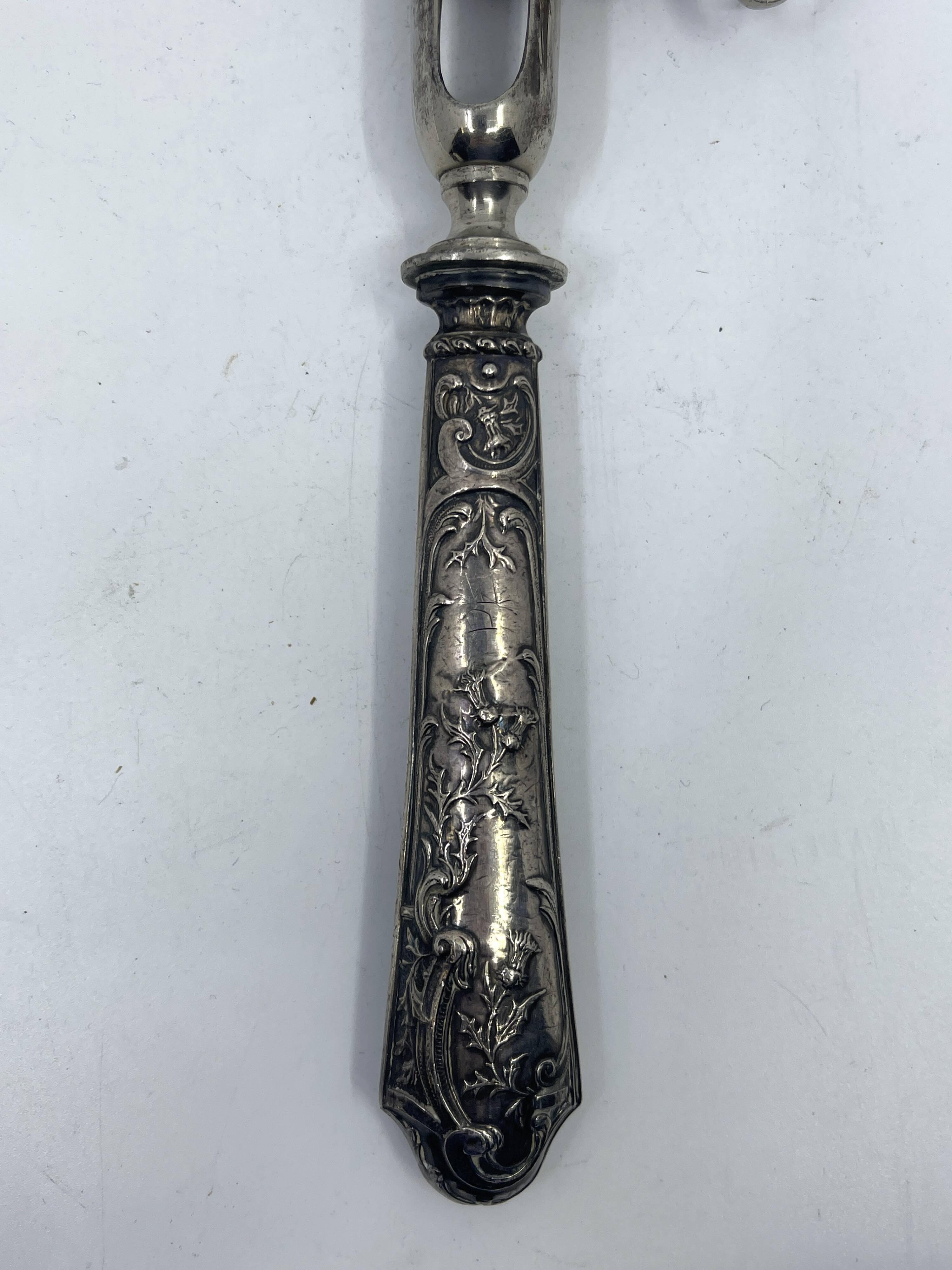 Silver-plated metal leg of lamb handle with engraved thistle flower patterns.