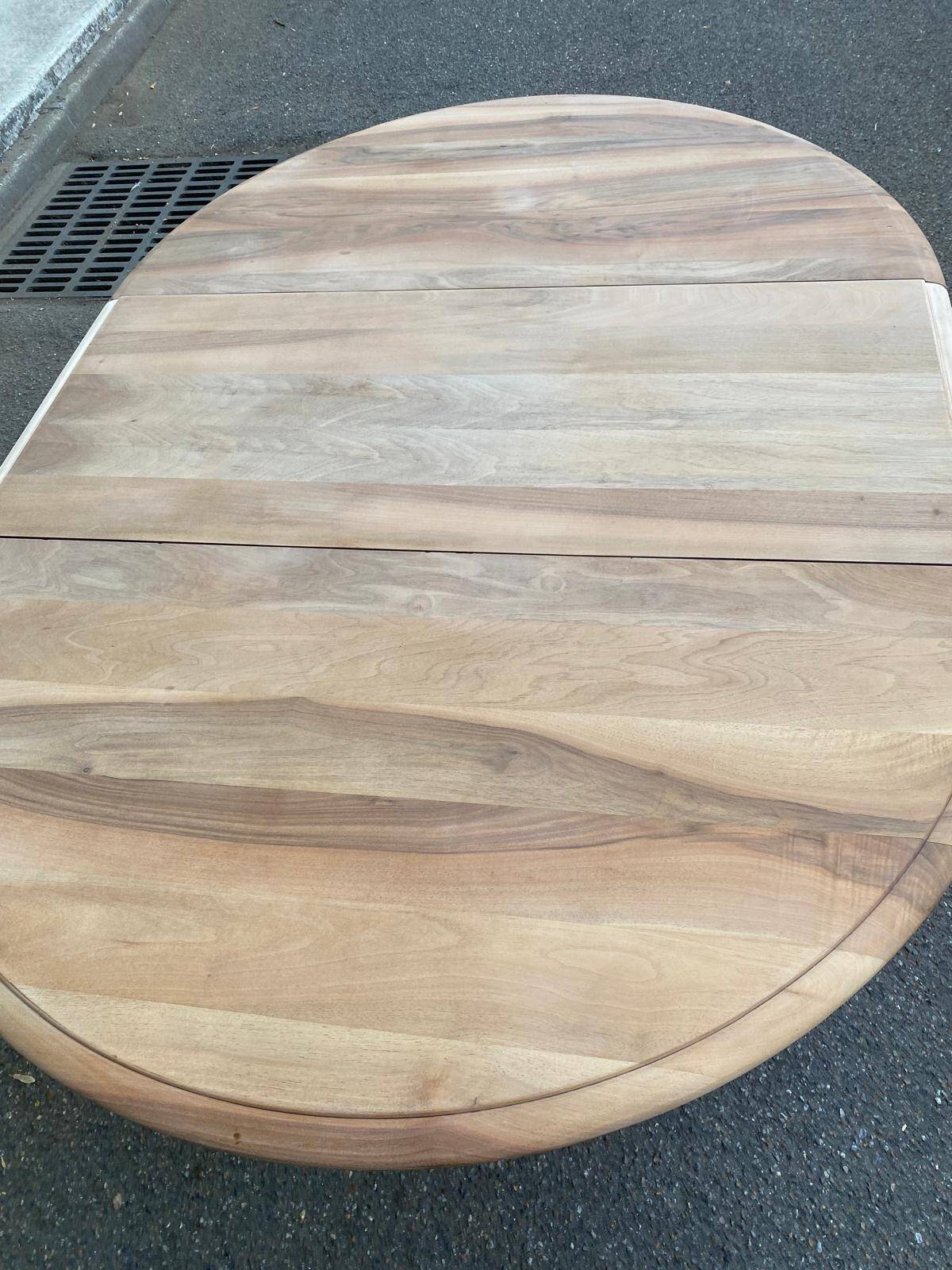 Round extendable dining table stripped in solid raw walnut with a central leg.