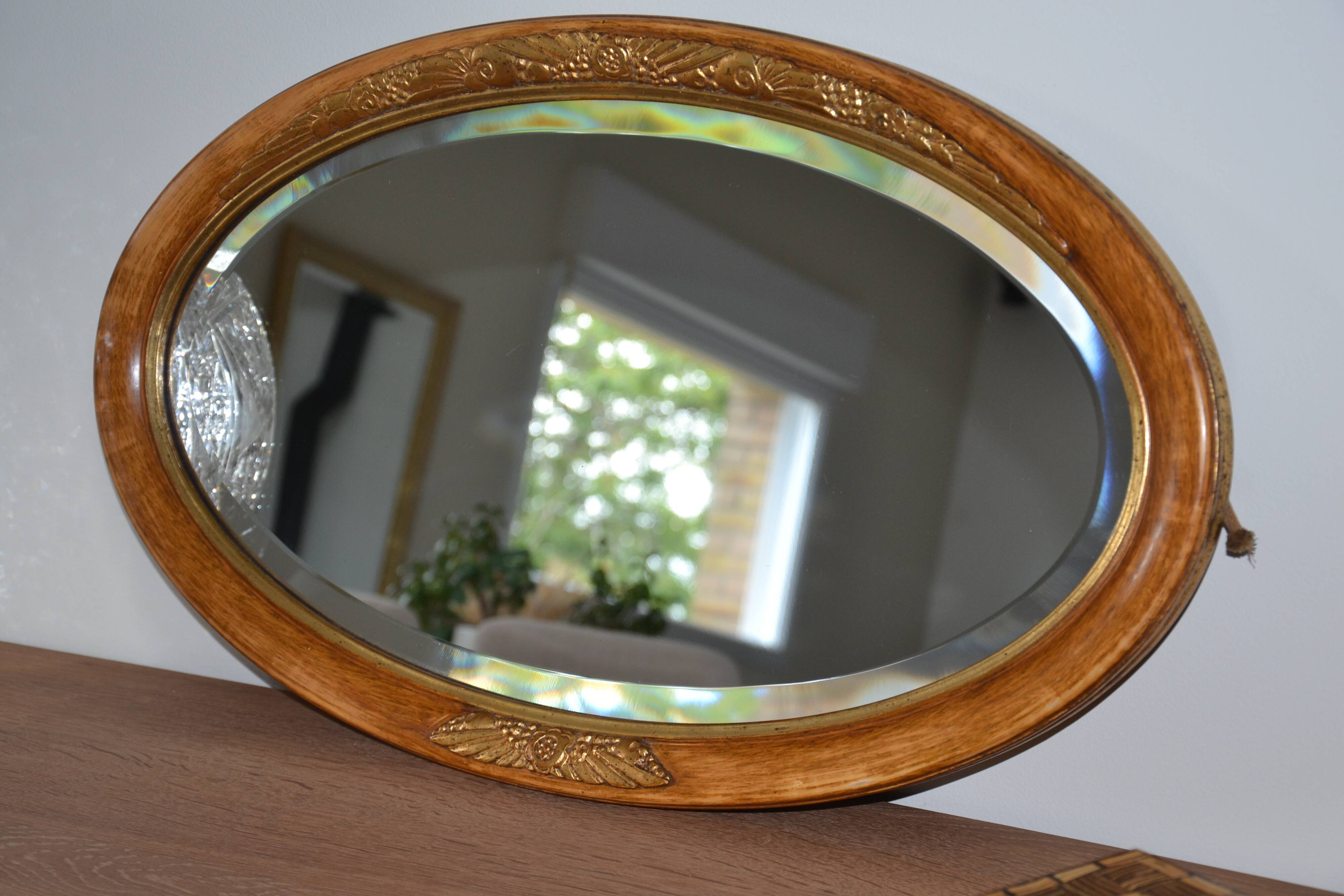 Old oval beveled wooden mirror, partly gilded and carved