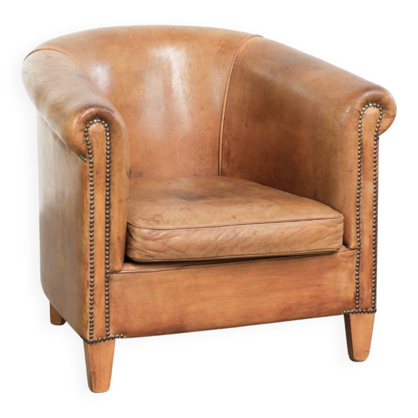 Fauteuil club en peau de mouton de couleur cognac, fini avec des clous décoratifs.