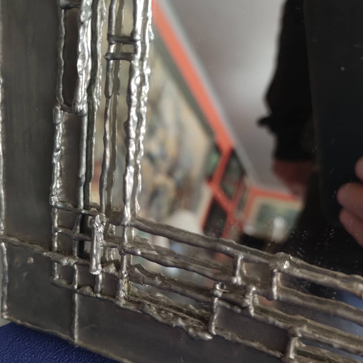 Pewter mirror on a brutalist-style wooden stand