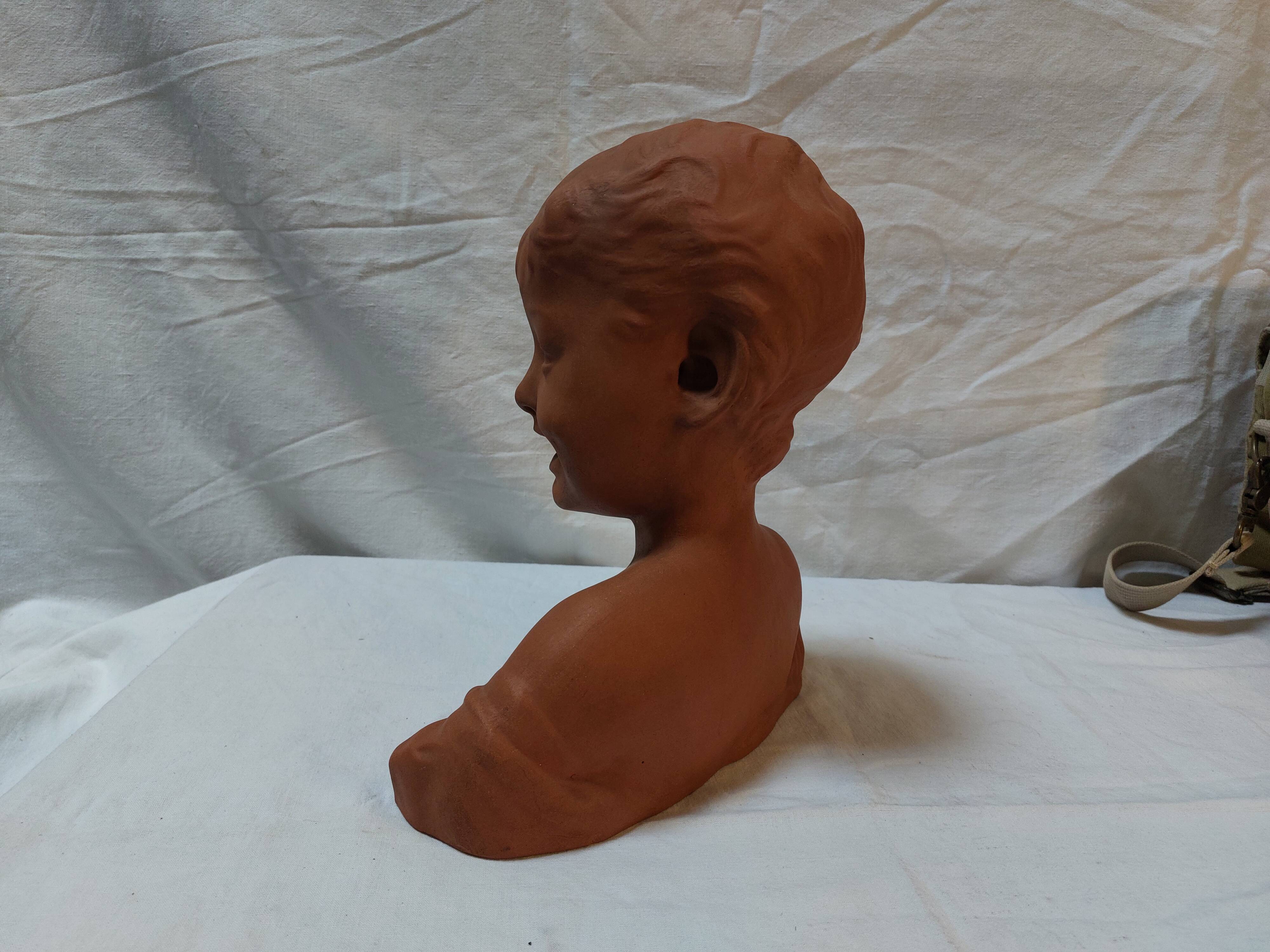 Terracotta bust of a smiling little boy.