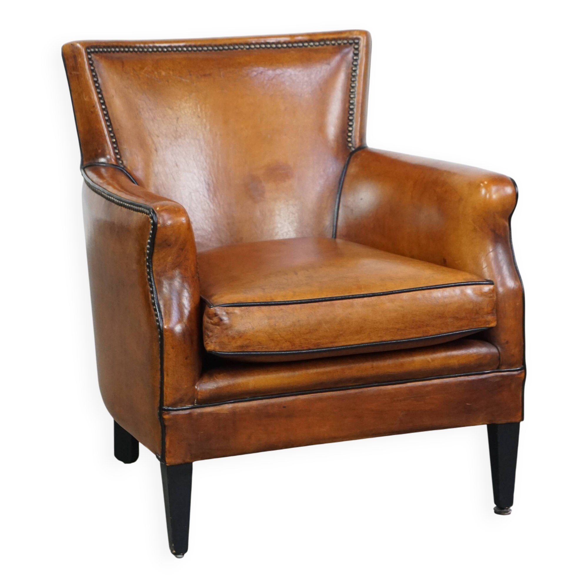 Cognac-colored sheepskin armchair with black piping and decorative nails