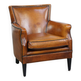 Cognac-colored sheepskin armchair with black piping and decorative nails