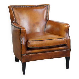 Cognac-colored sheepskin armchair with black piping and decorative nails