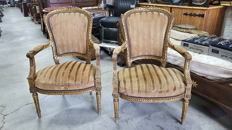 A pair of gilded wooden armchairs in the Louis XVI style.