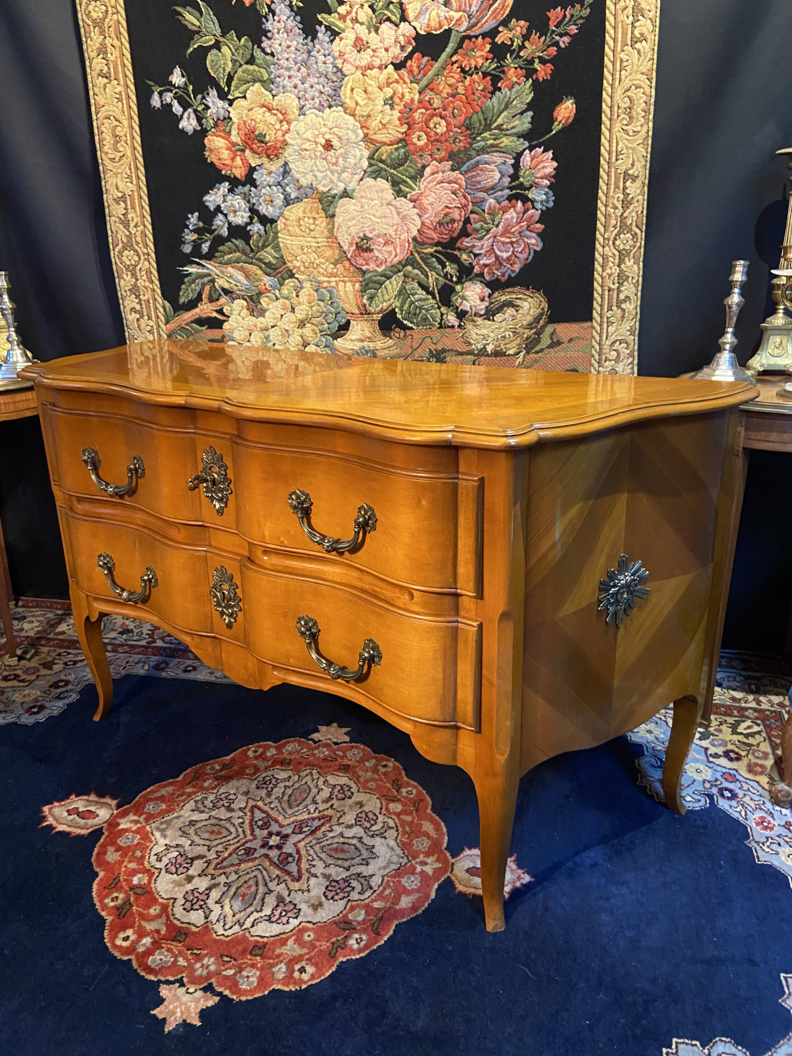 Large bow-fronted chest of drawers in blonde cherry with bronze ornamentation.