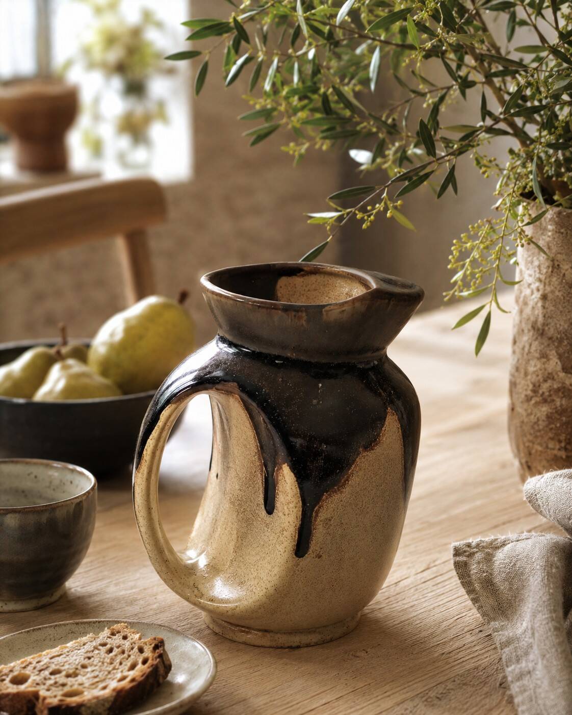 Stoneware jug with deep black drips on a sandy background.