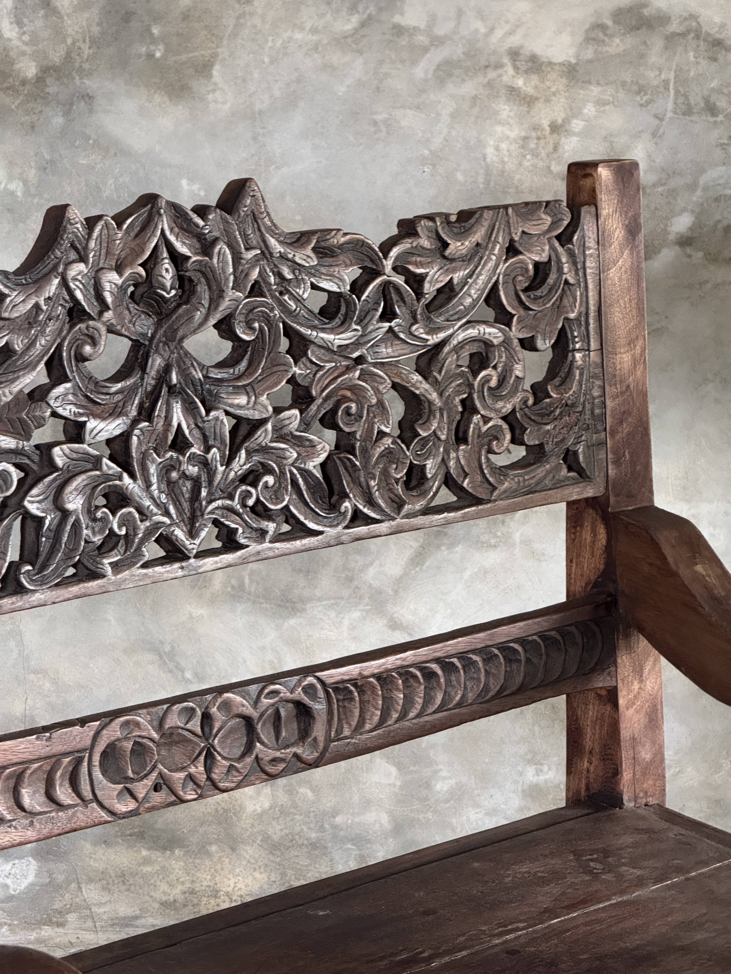 Small antique Indonesian bench in carved teak with plant and floral motifs.