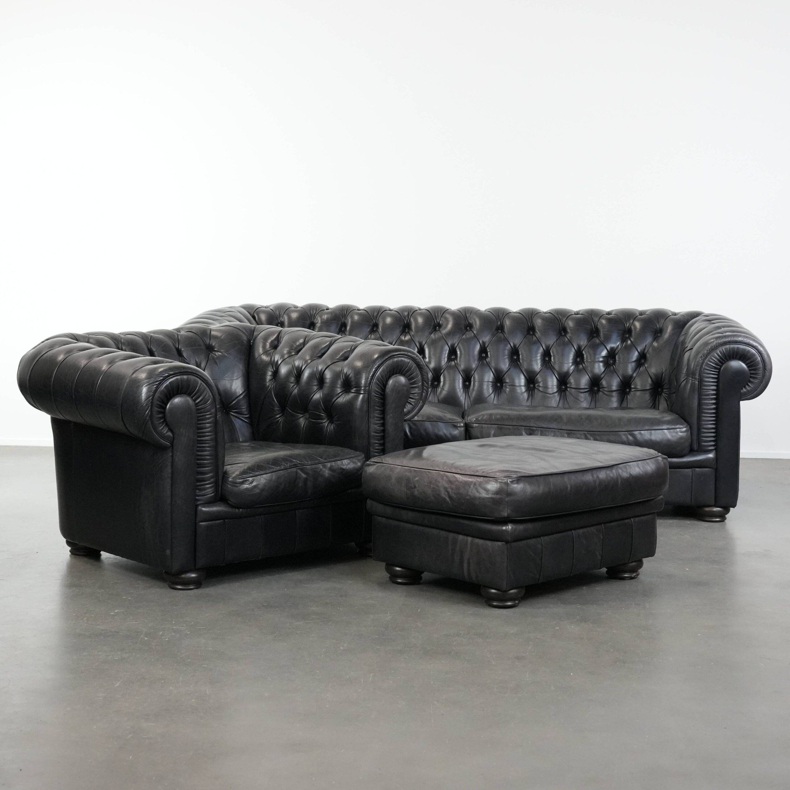 Ensemble composé d'un canapé chesterfield noir, d'un fauteuil et d'un pouf.