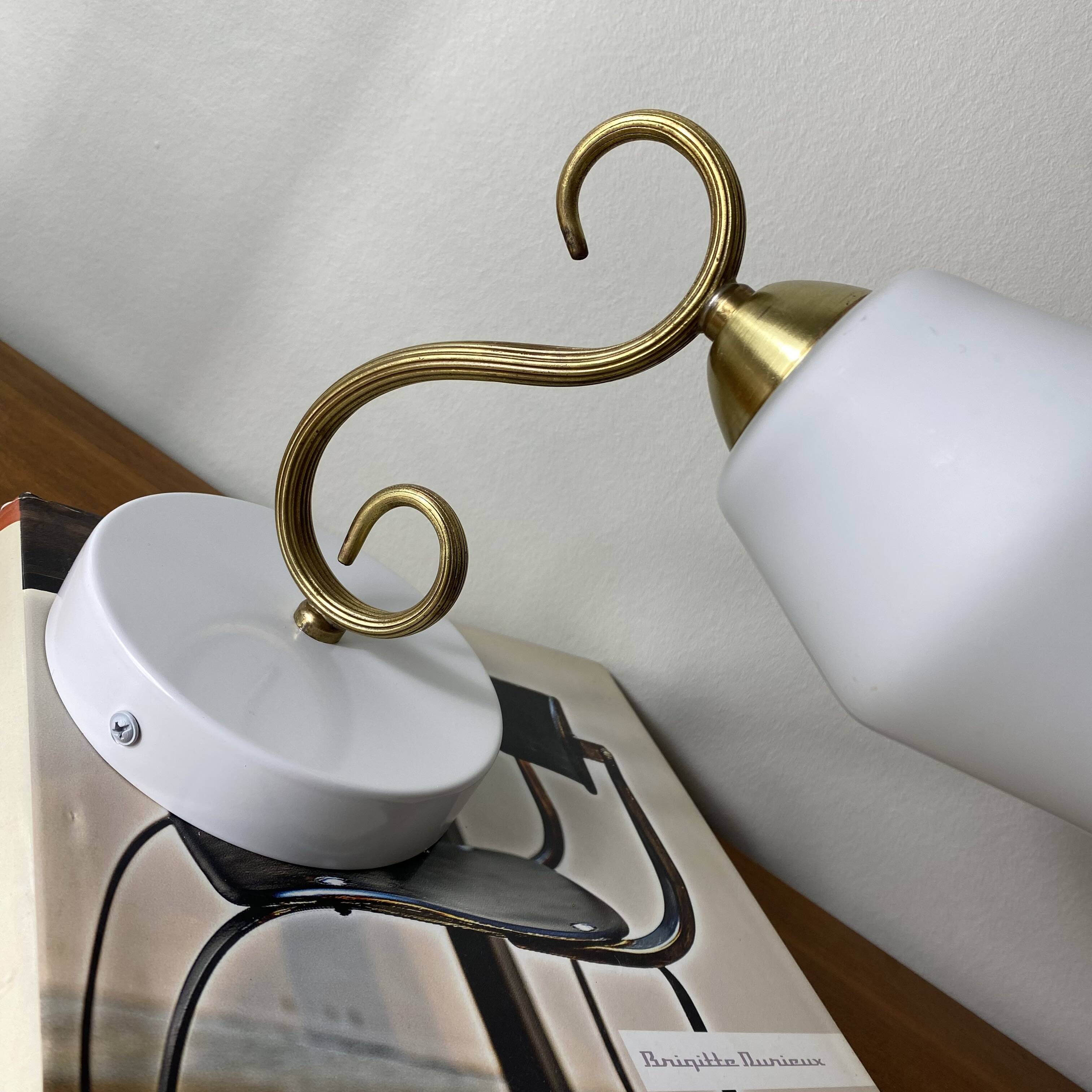 Swan neck wall light in brass with a white glass shade.