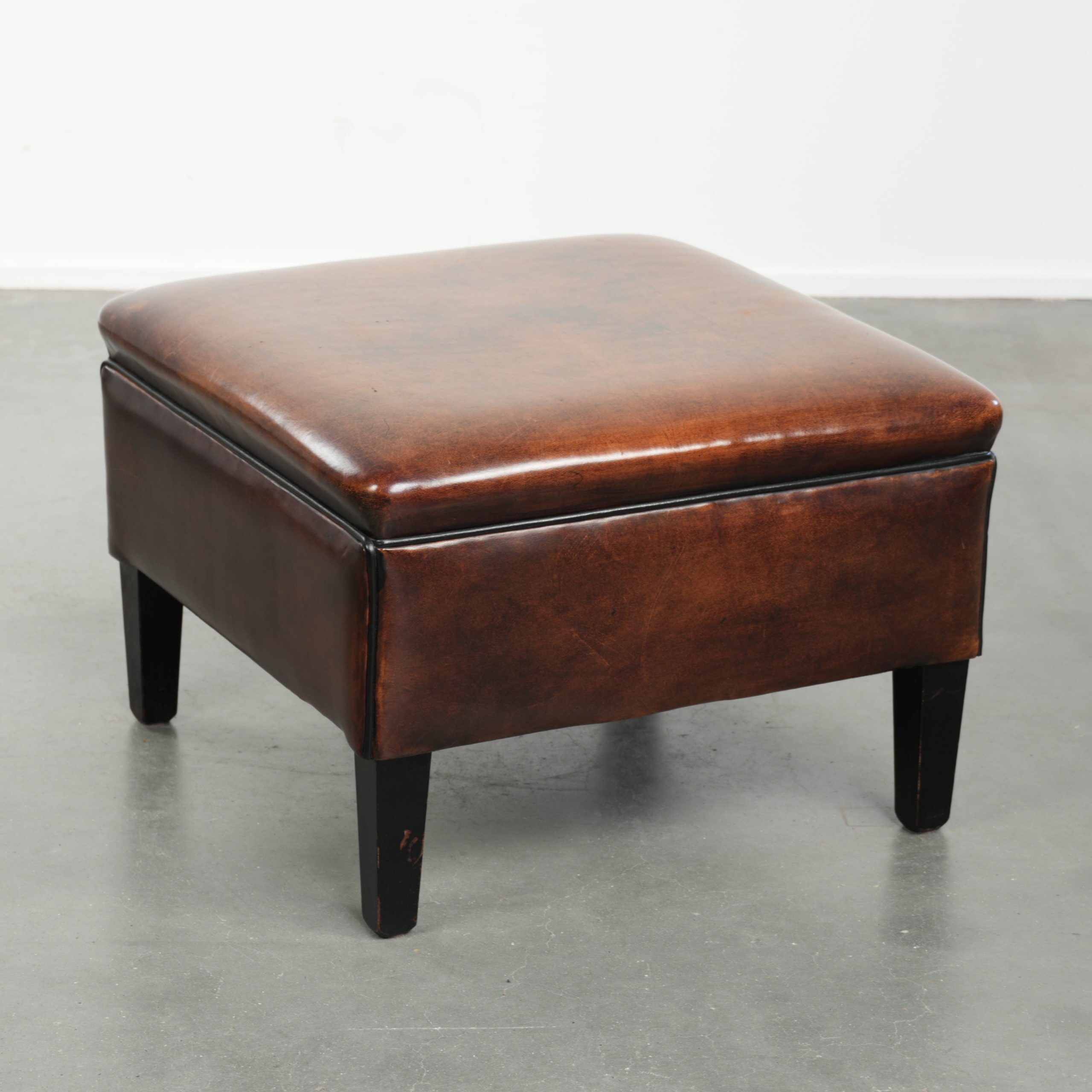 Large dark brown square ottoman made of sheepskin with black piping