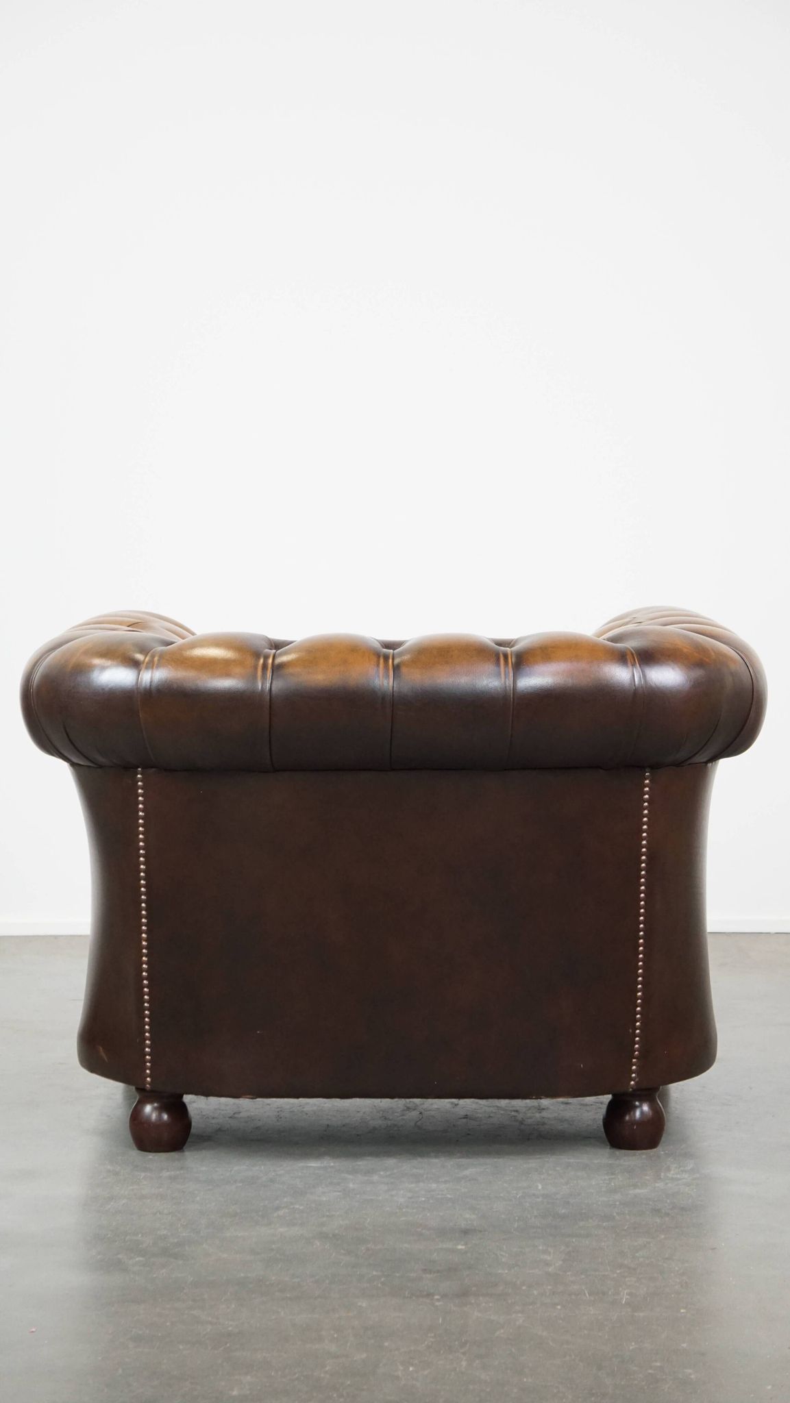 A well-maintained cowhide leather English Chesterfield armchair