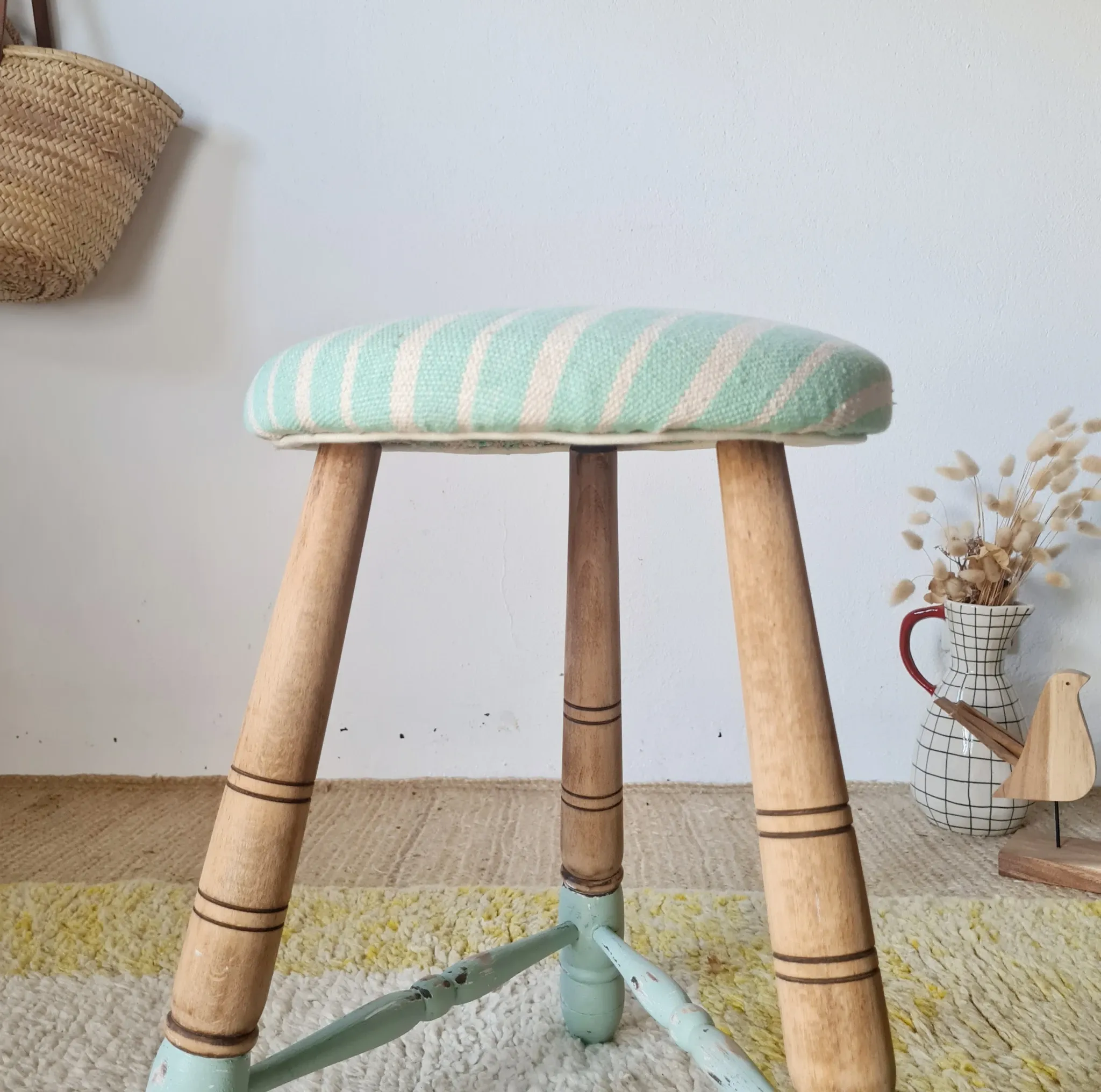 Antique tripod stool with blue striped seat.