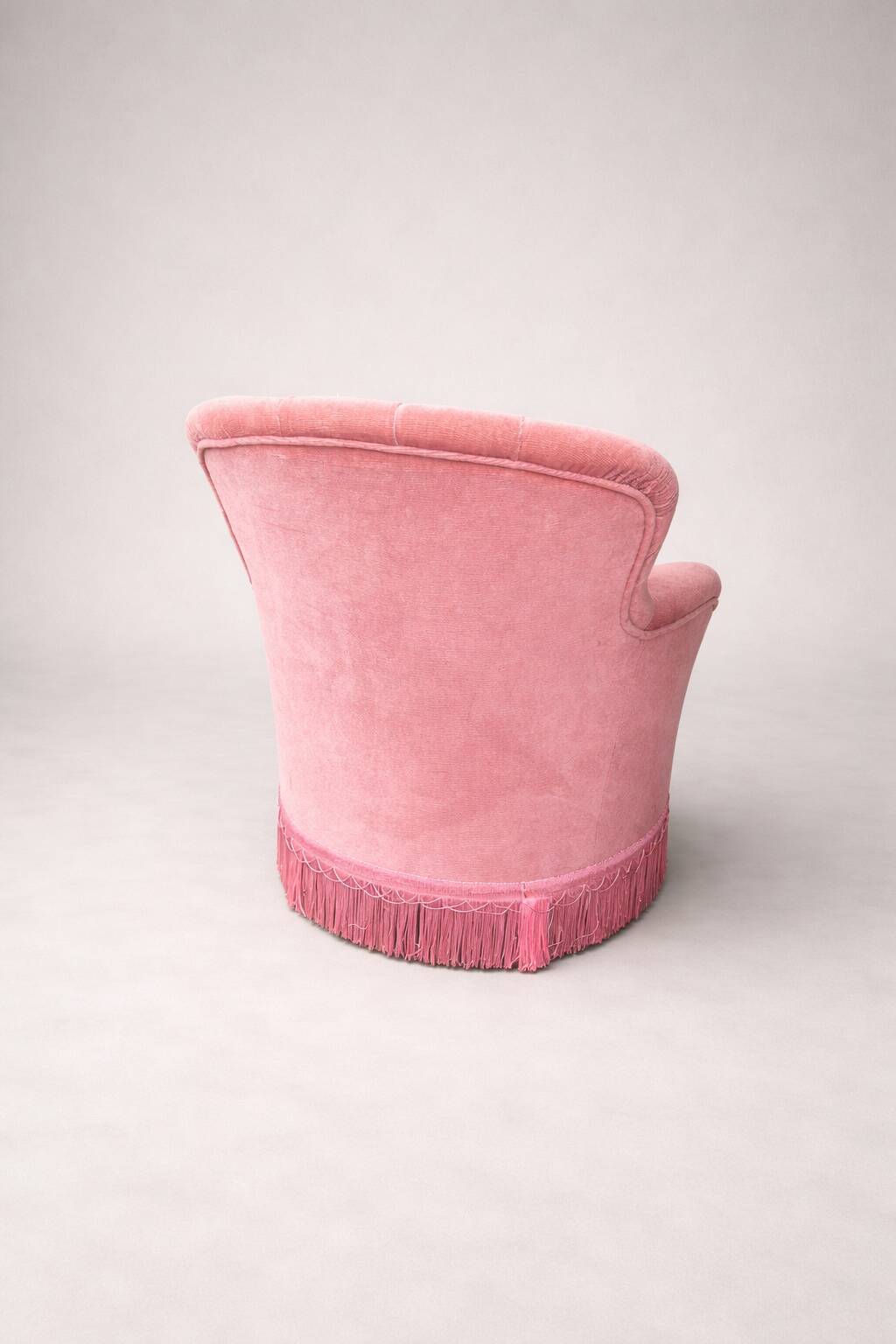Vintage pink velvet tufted armchair with fringes.