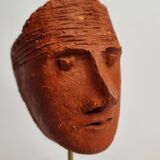 Stylized head in patinated ochre terracotta on a dark wooden base, 17 cm