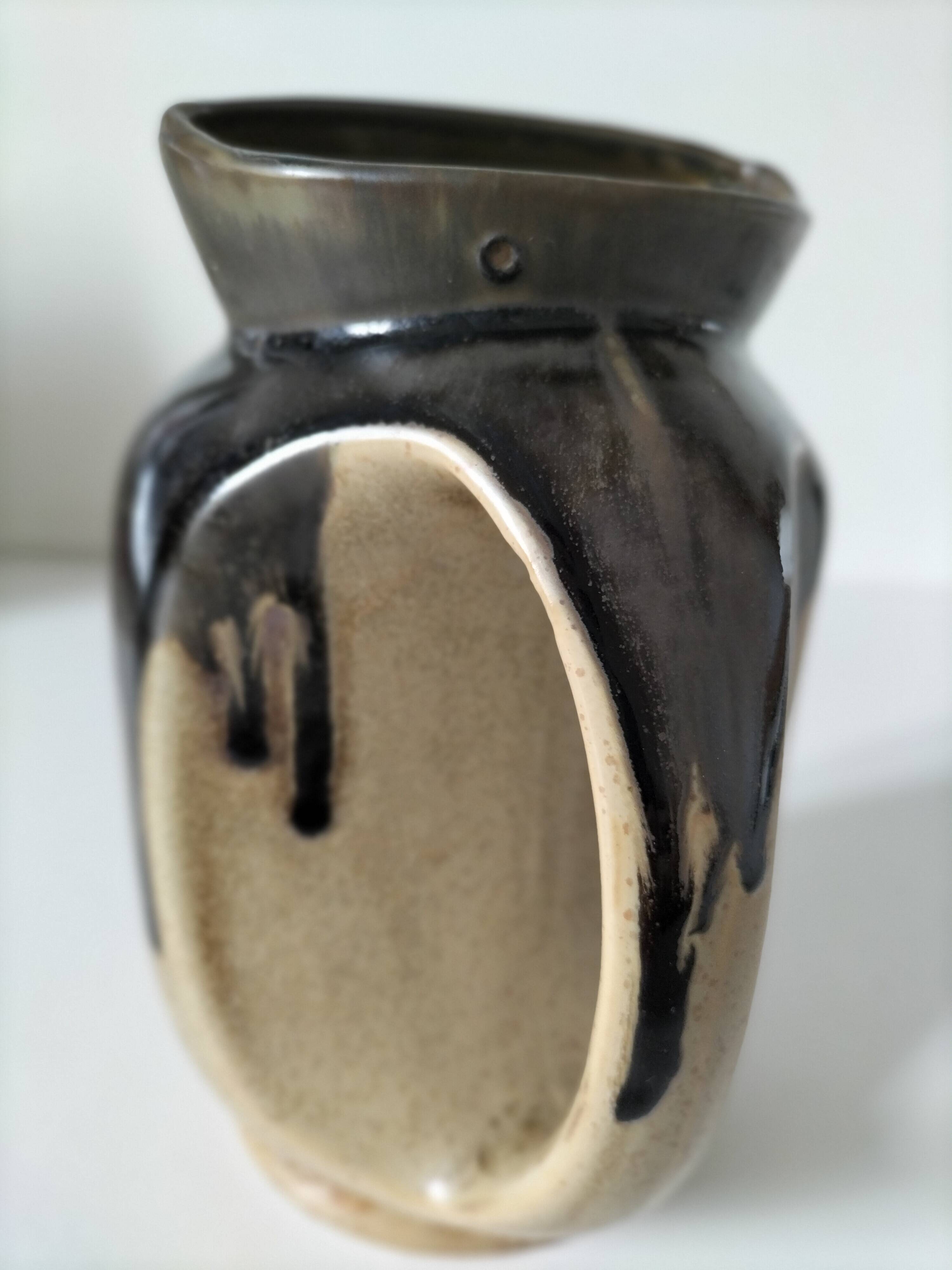 Stoneware jug with deep black drips on a sandy background.