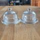 2 transparent glass butter dishes with their matching cloches.
