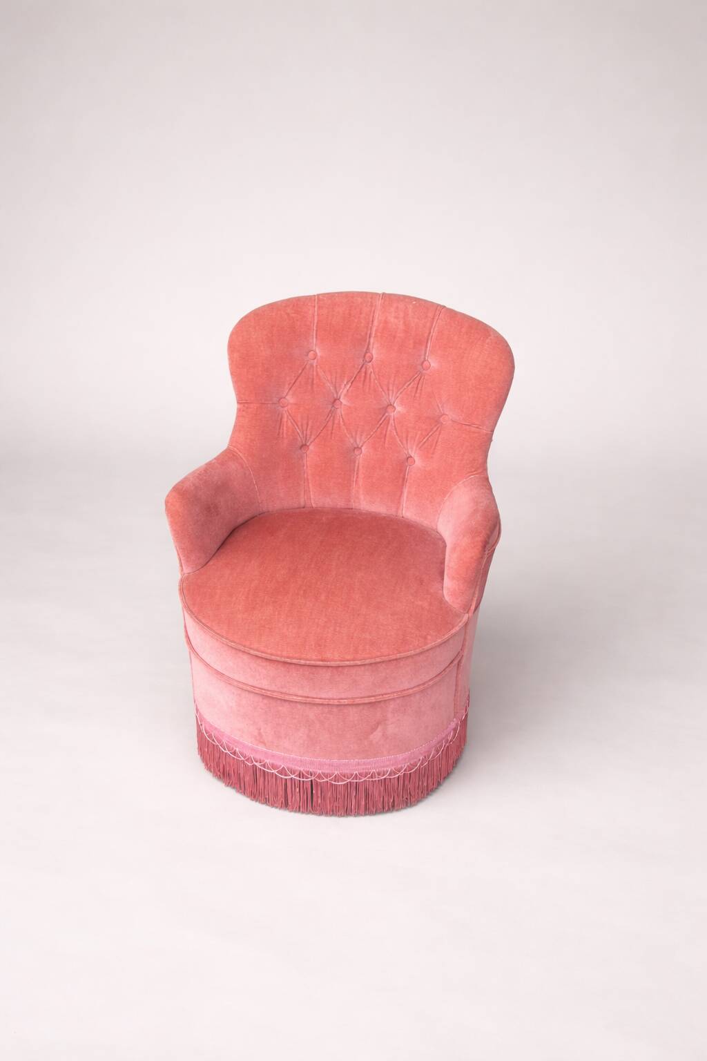 Vintage pink velvet tufted armchair with fringes.