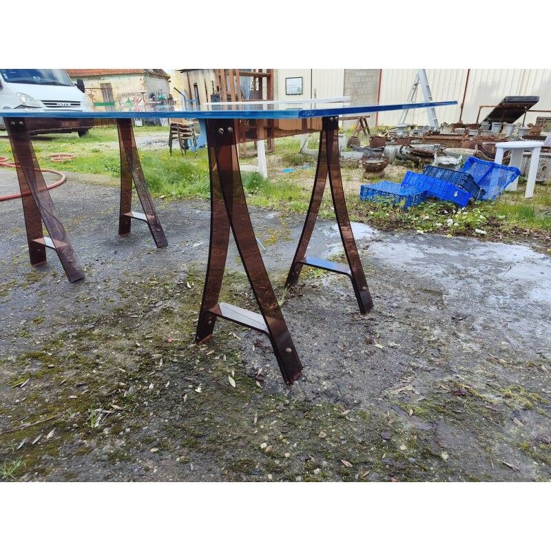 Vintage table with a glass top and smoked plastic trestle legs.