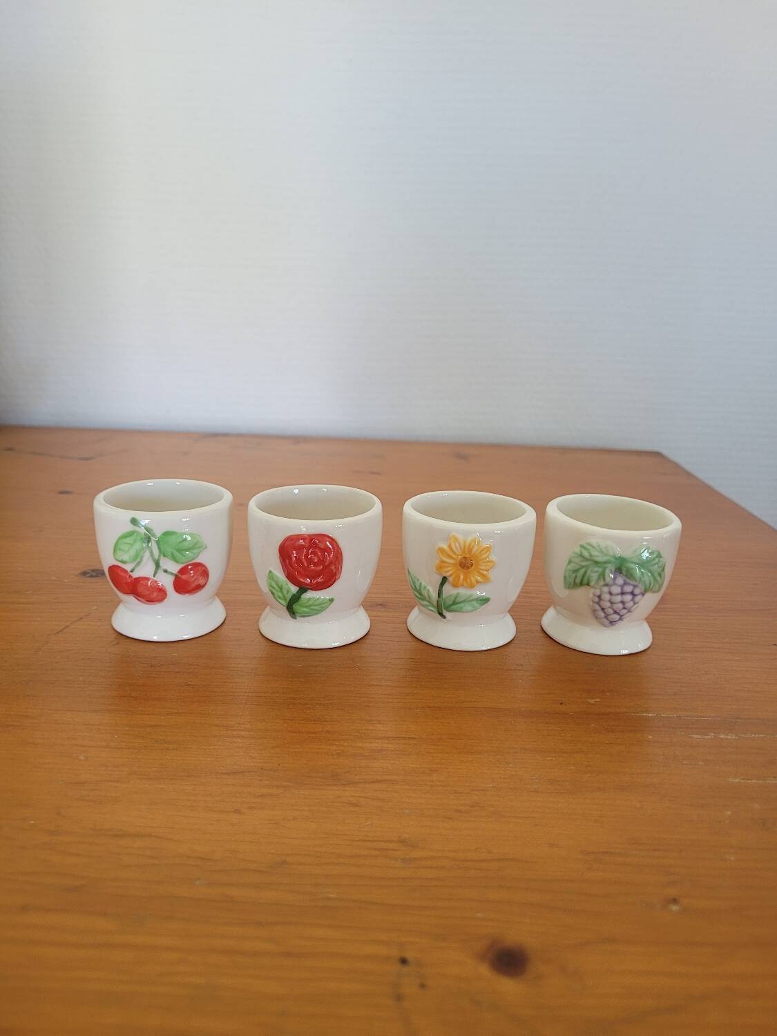 Set of four ceramic egg cups with a floral and fruit pattern.