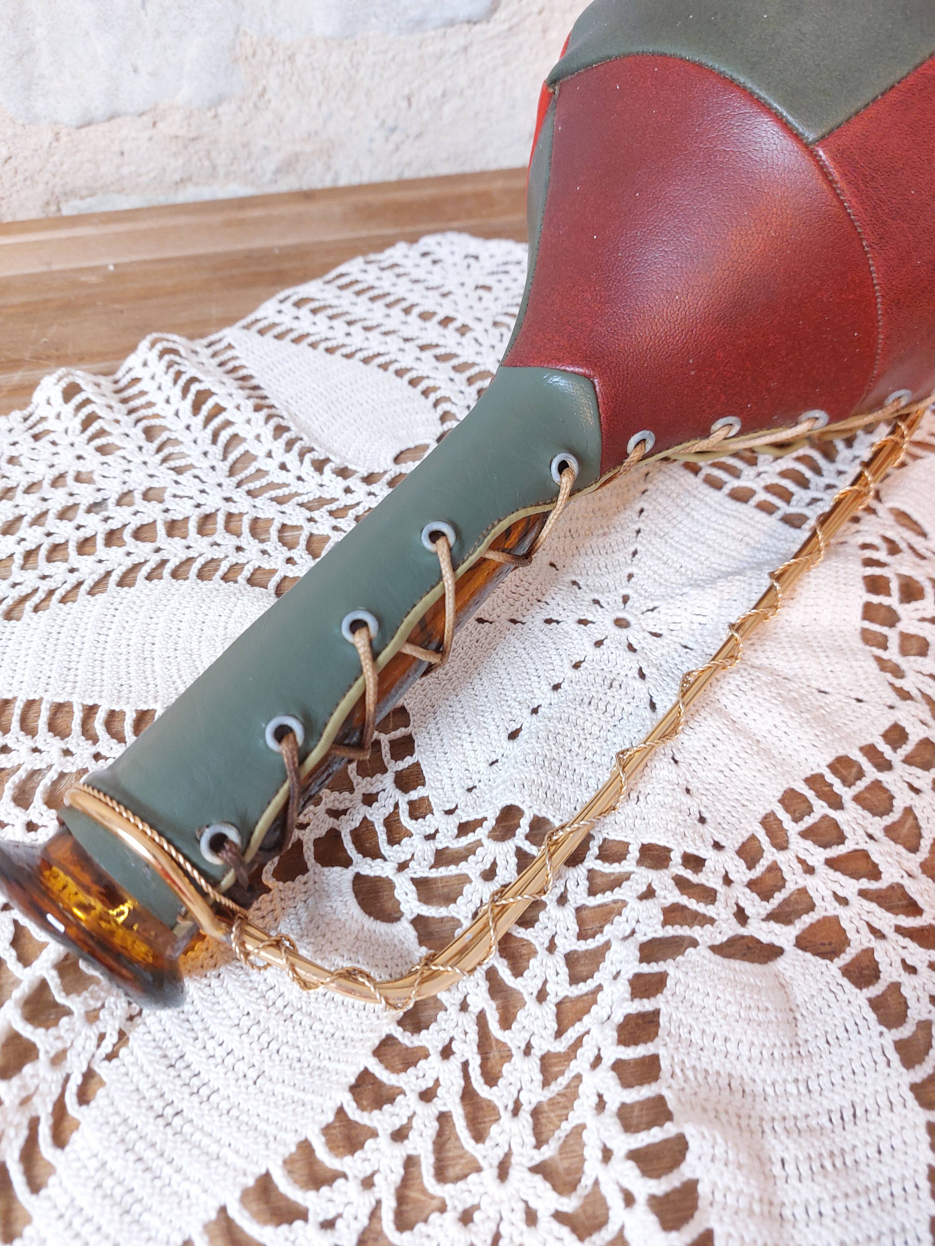 Amber bottle covered in colored leather with handle surrounded by wire, vintage