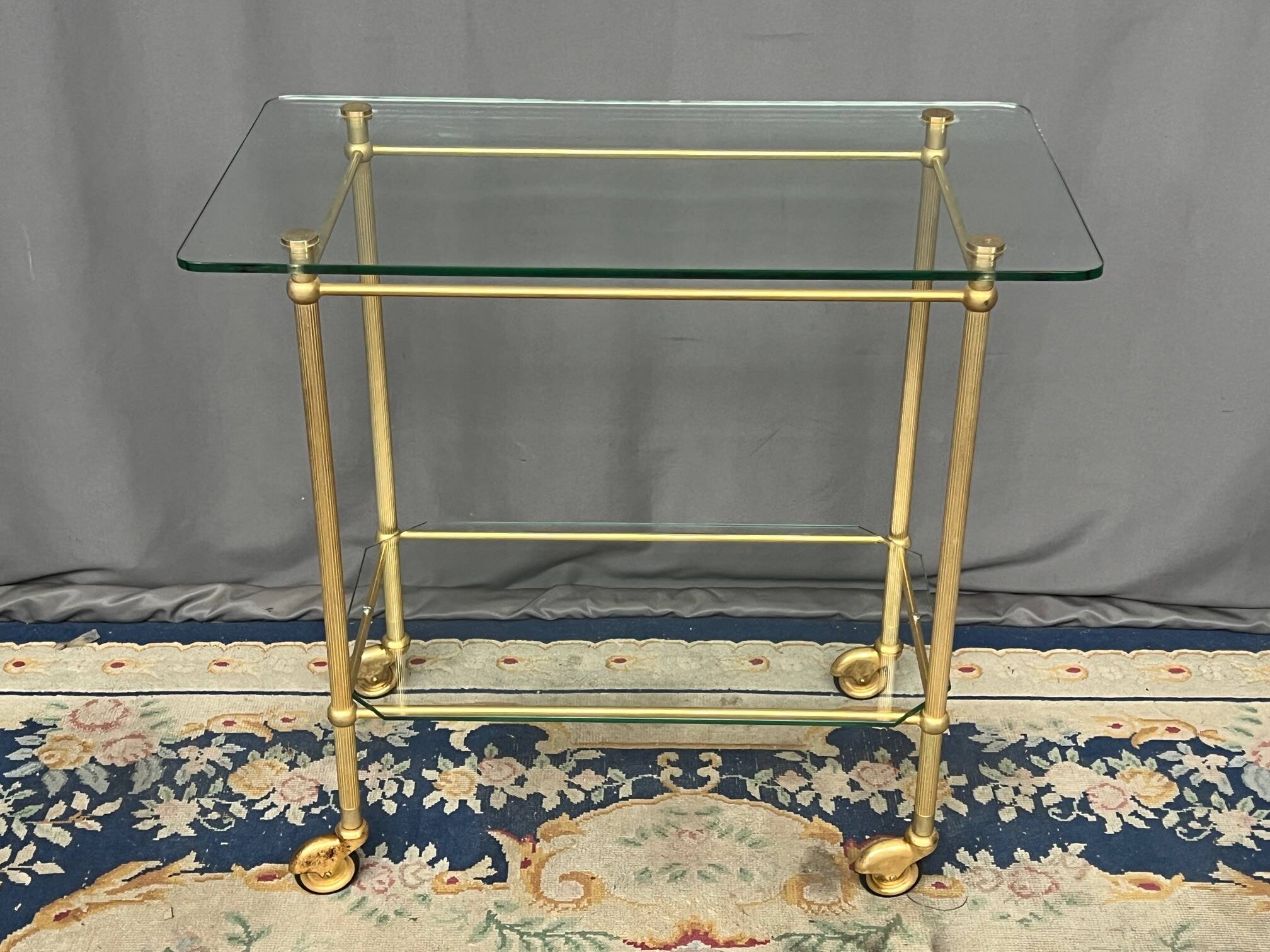 Service trolley on wheels with two glass shelves and a brass frame.