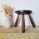 Small brutalist tripod stool made of turned wood.