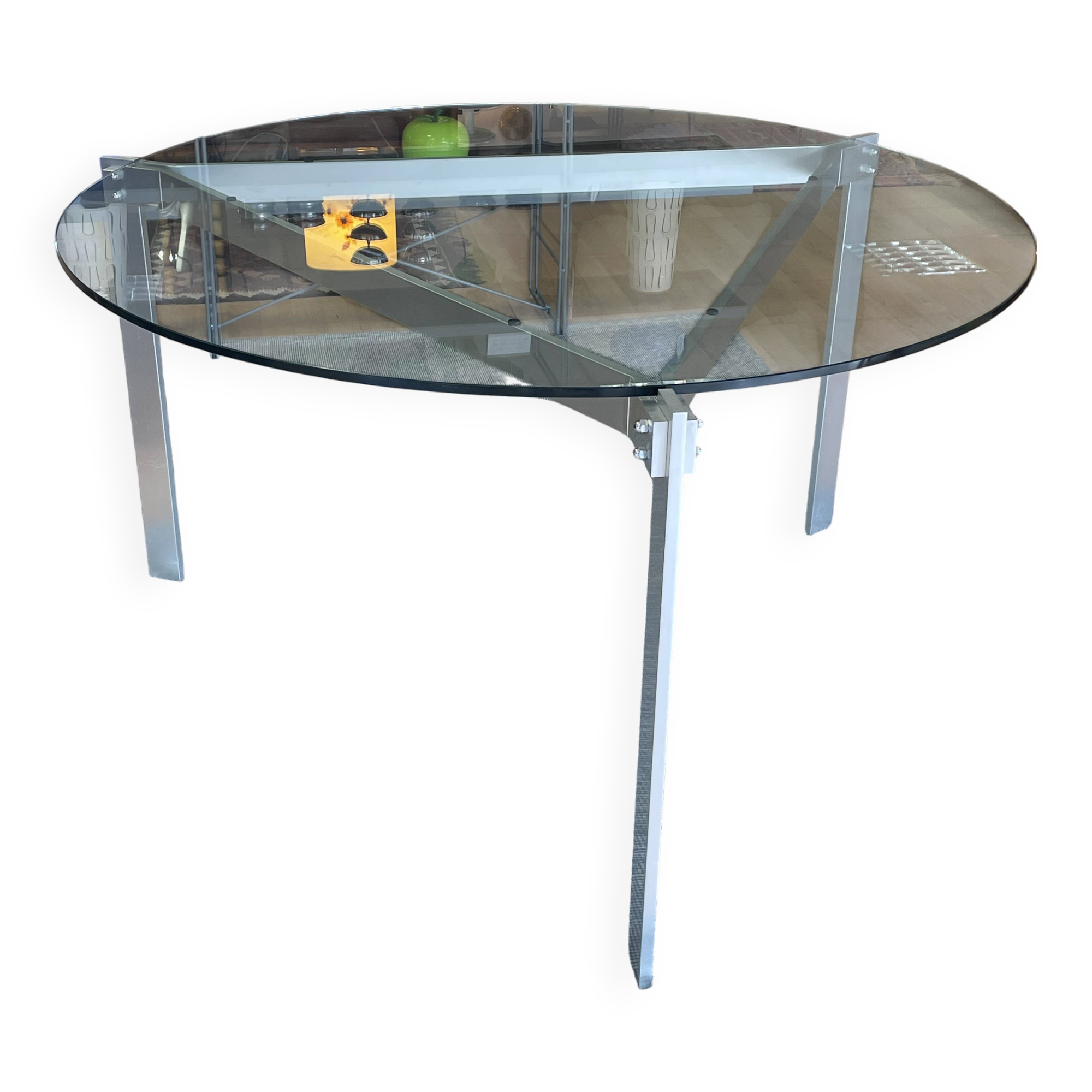Round dining table with a glass top and brushed metal triangular frame.