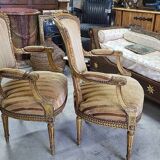 A pair of gilded wooden armchairs in the Louis XVI style.
