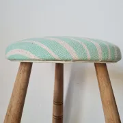 Antique tripod stool with blue striped seat.
