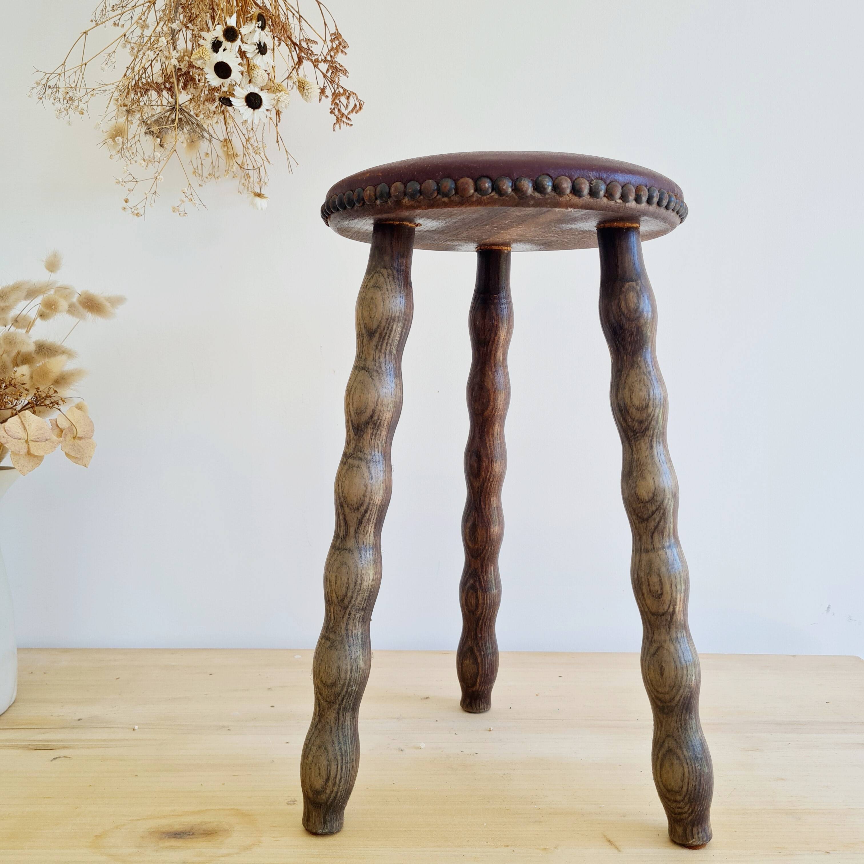 Antique tripod stool with turned wooden legs and leather seat.