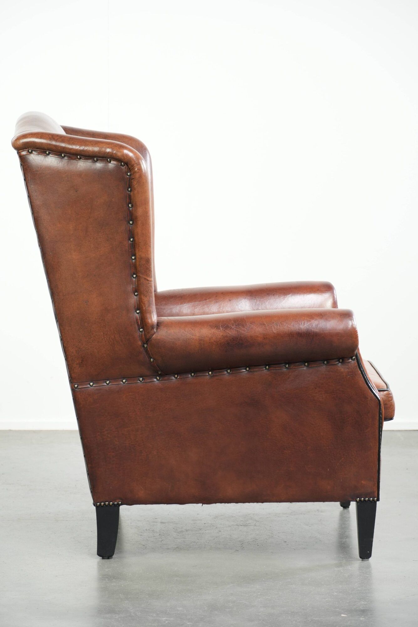 Sheepskin wingback armchair in a warm cognac colour with refined nailhead trim