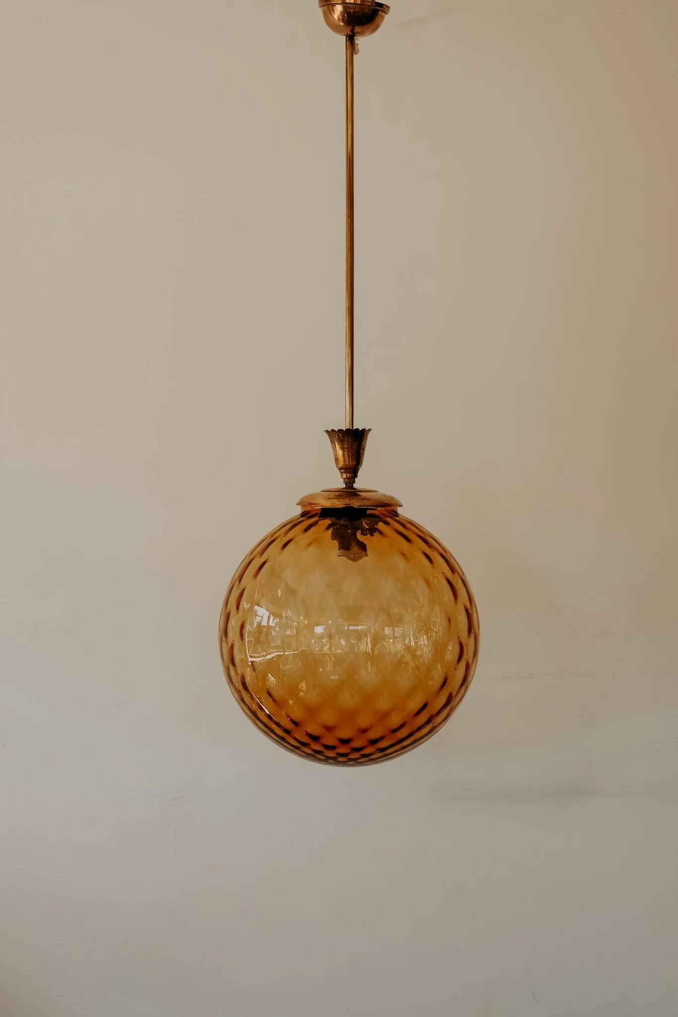 Brass pendant light with a round orange glass shade and a swirling structure.