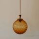 Brass pendant light with a round orange glass shade and a swirling structure.