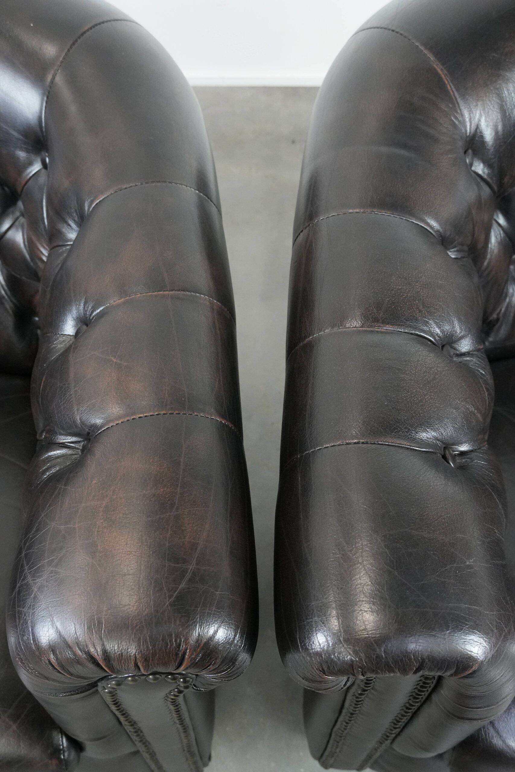 Ensemble de deux luxueux fauteuils club Chesterfield en cuir de vachette noir.