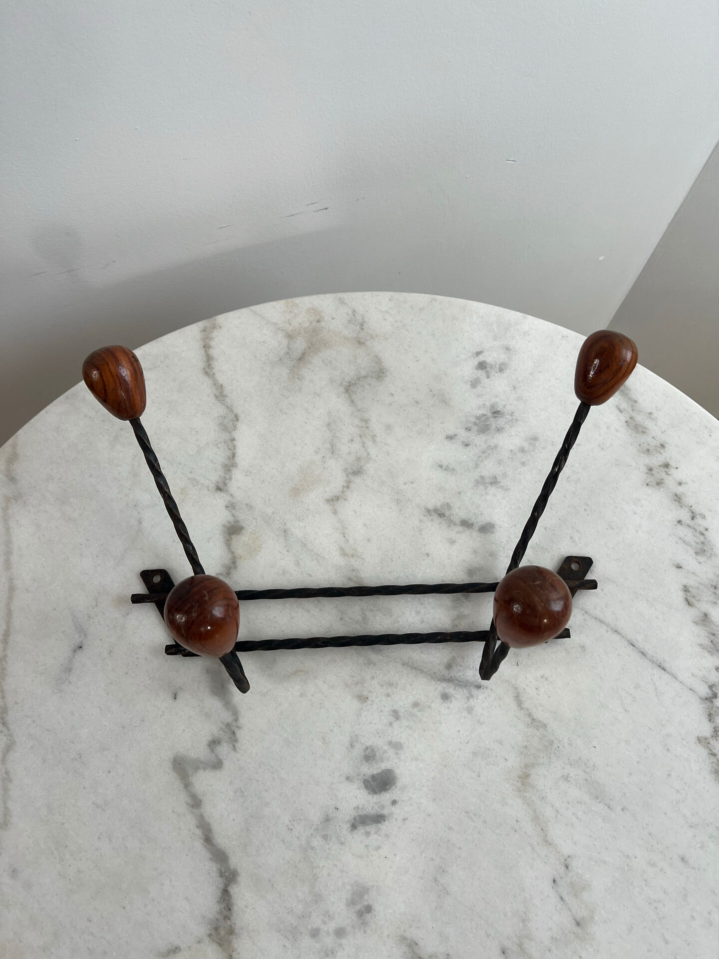 Wall-mounted coat rack in wrought iron with turned wooden knobs.