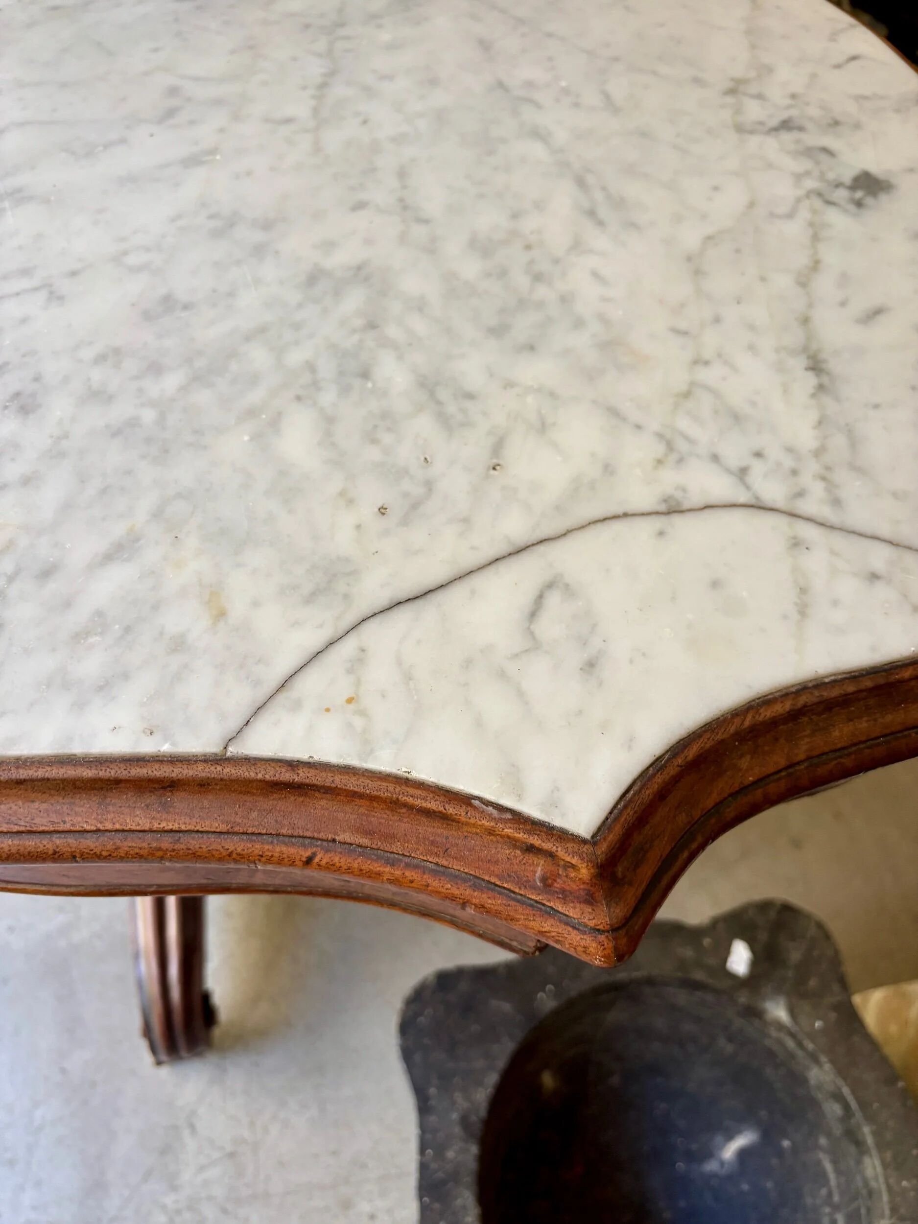 Table with a carved wooden frame and grey marble top on wheels, measuring 130 x 82 cm.