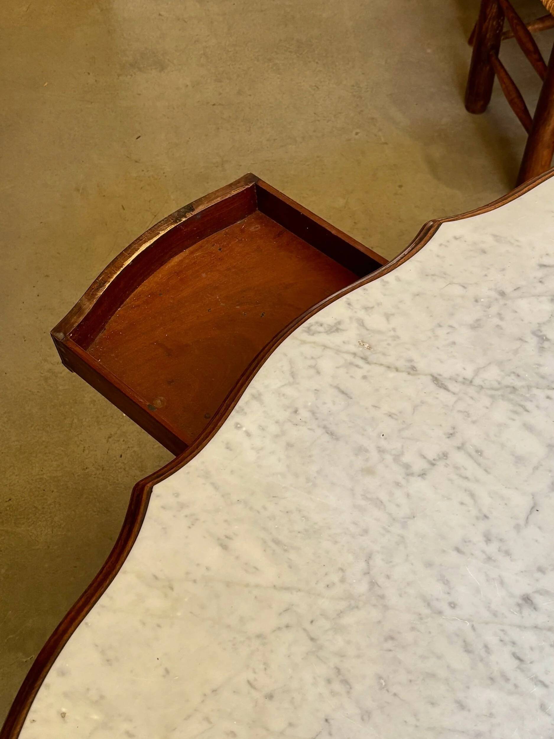 Table with a carved wooden frame and grey marble top on wheels, measuring 130 x 82 cm.