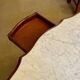 Table with a carved wooden frame and grey marble top on wheels, measuring 130 x 82 cm.