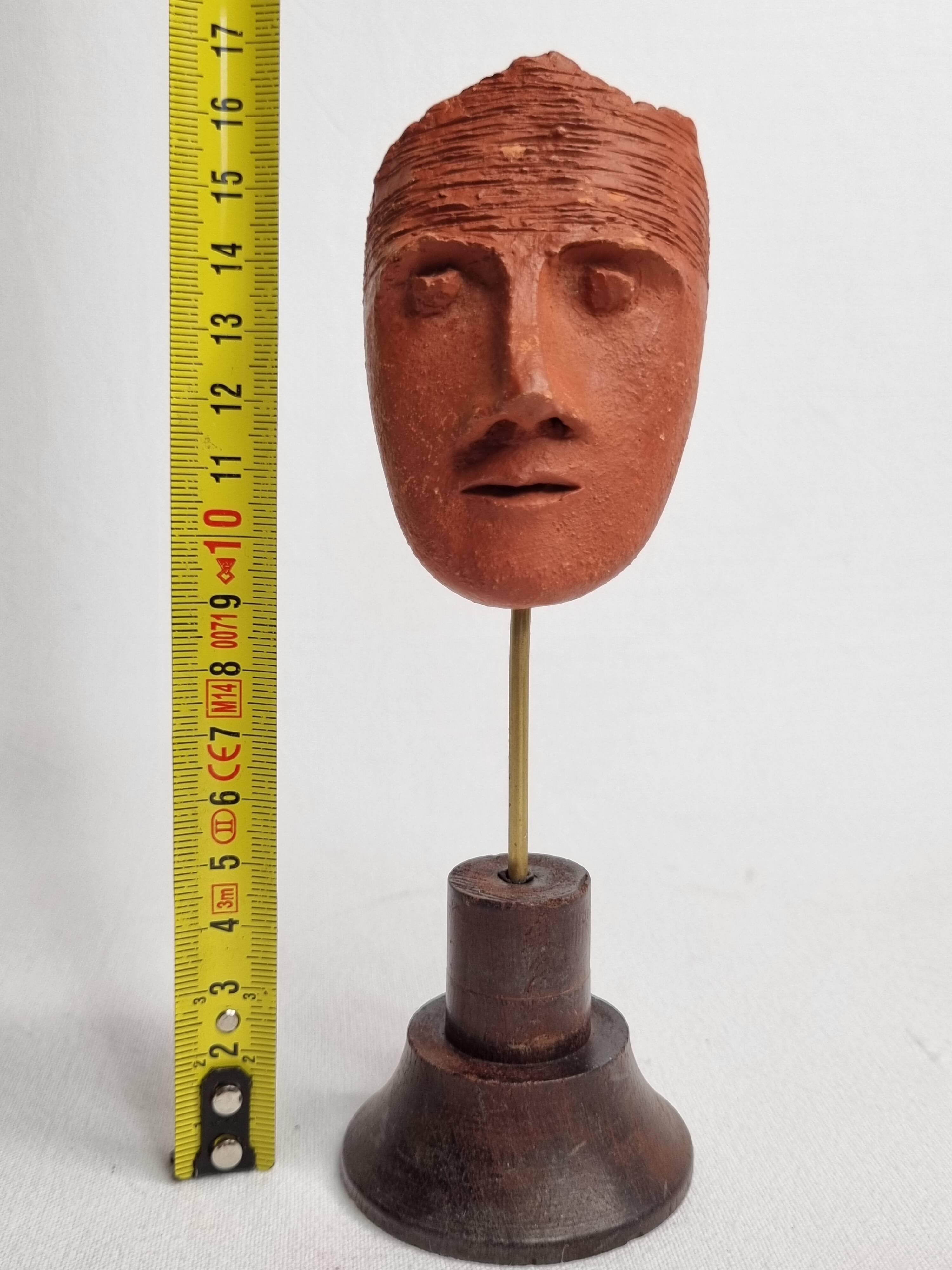 Stylized head in patinated ochre terracotta on a dark wooden base, 17 cm
