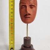 Stylized head in patinated ochre terracotta on a dark wooden base, 17 cm