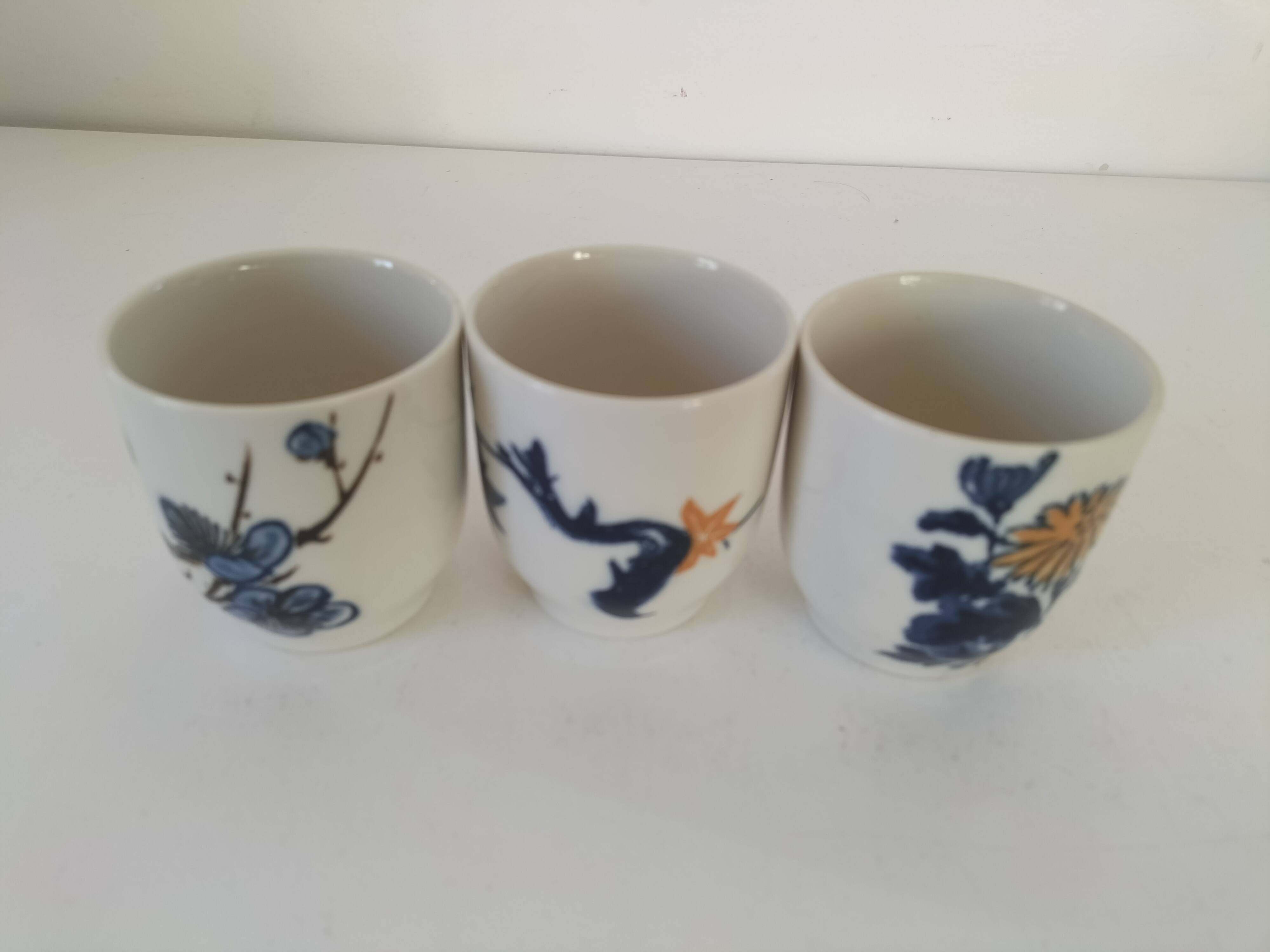 Set of three hand-painted porcelain cups with floral patterns.