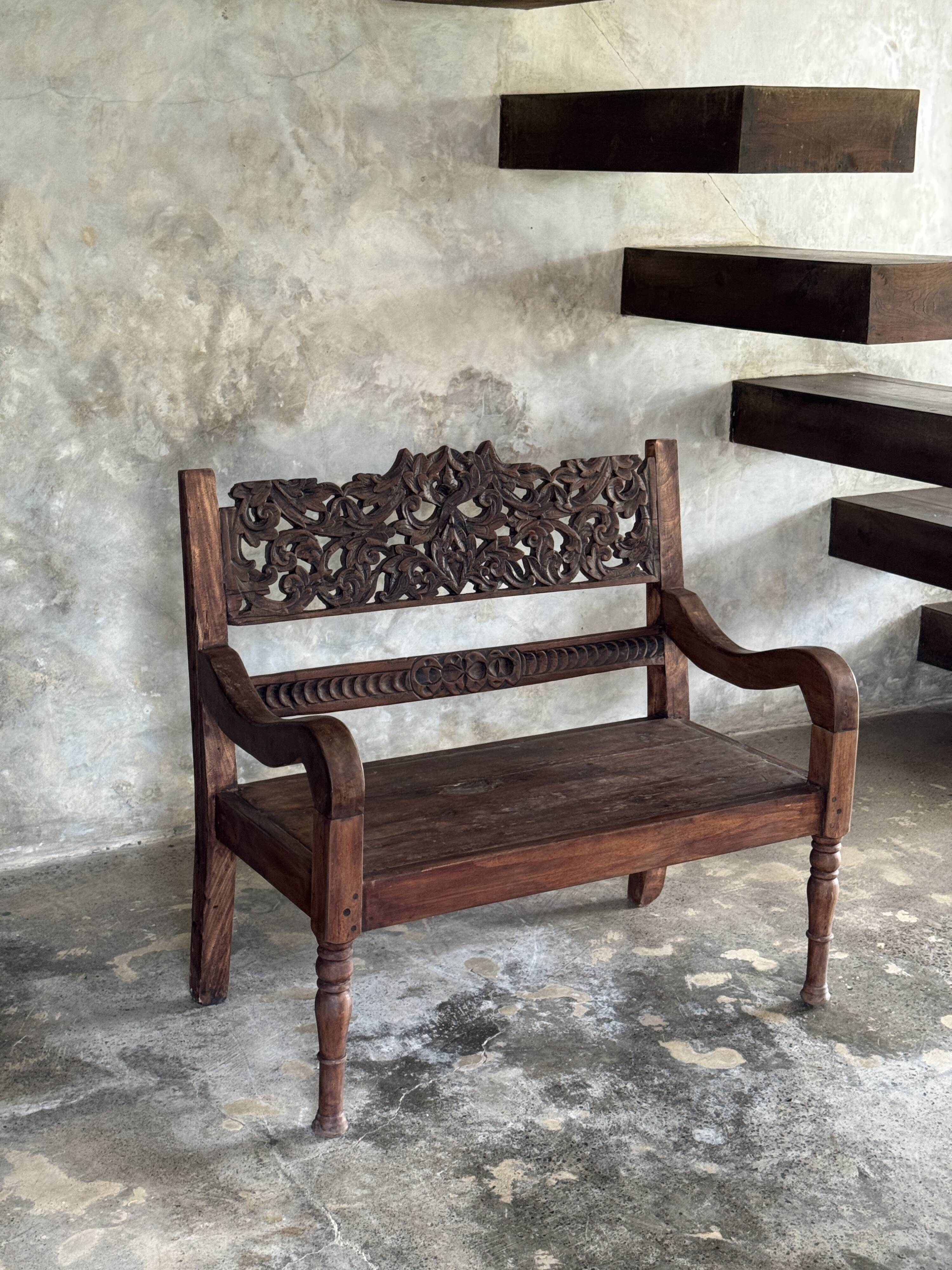 Small antique Indonesian bench in carved teak with plant and floral motifs.