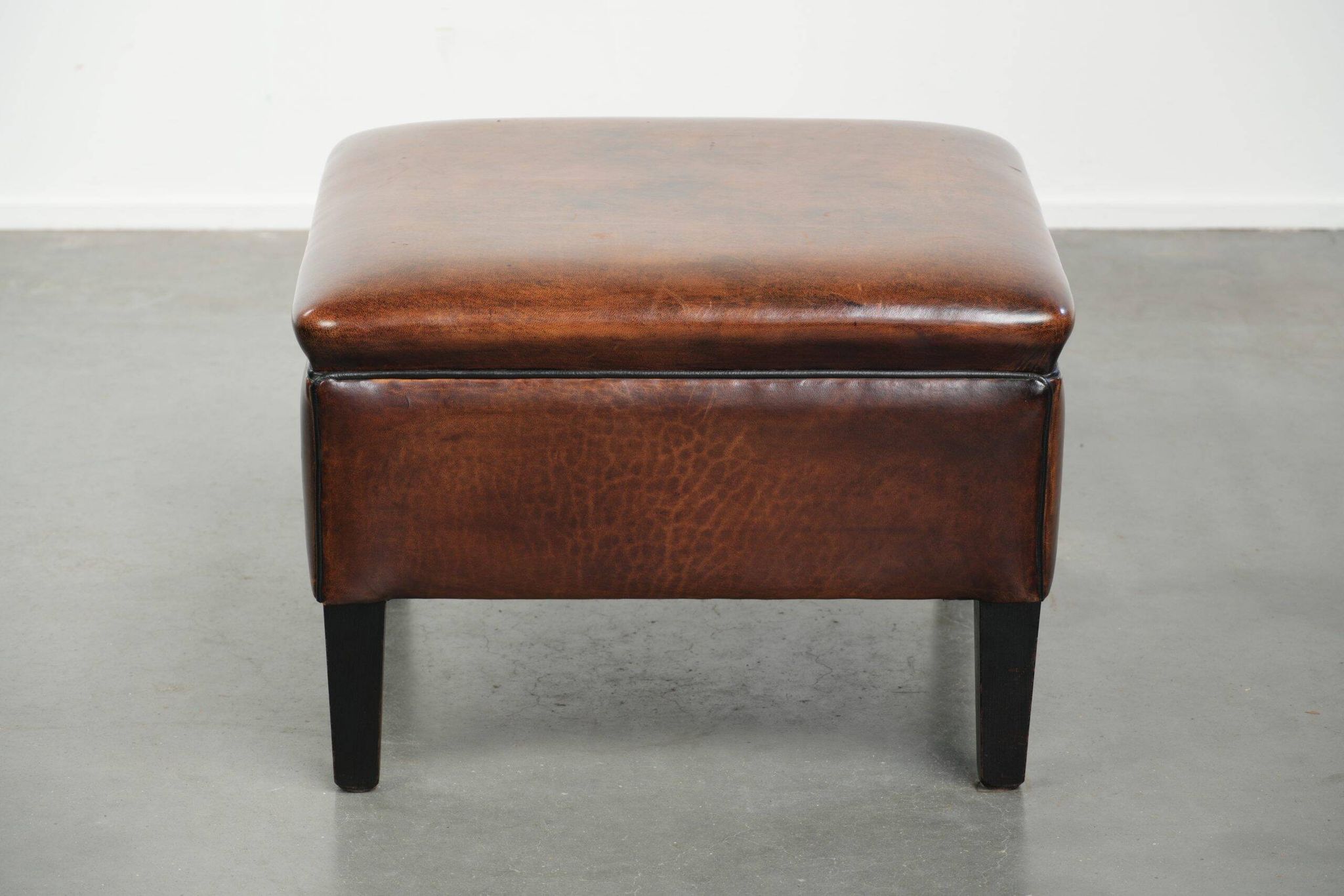 Pouf carré marron foncé en peau de mouton avec un passepoil noir.
