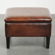 Pouf carré marron foncé en peau de mouton avec un passepoil noir.