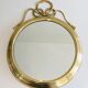 Decorative oval mirror in brass adorned with a large twisted bow.