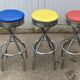 Set of 5 vintage swivel bar stools in blue, red, orange, and yellow.
