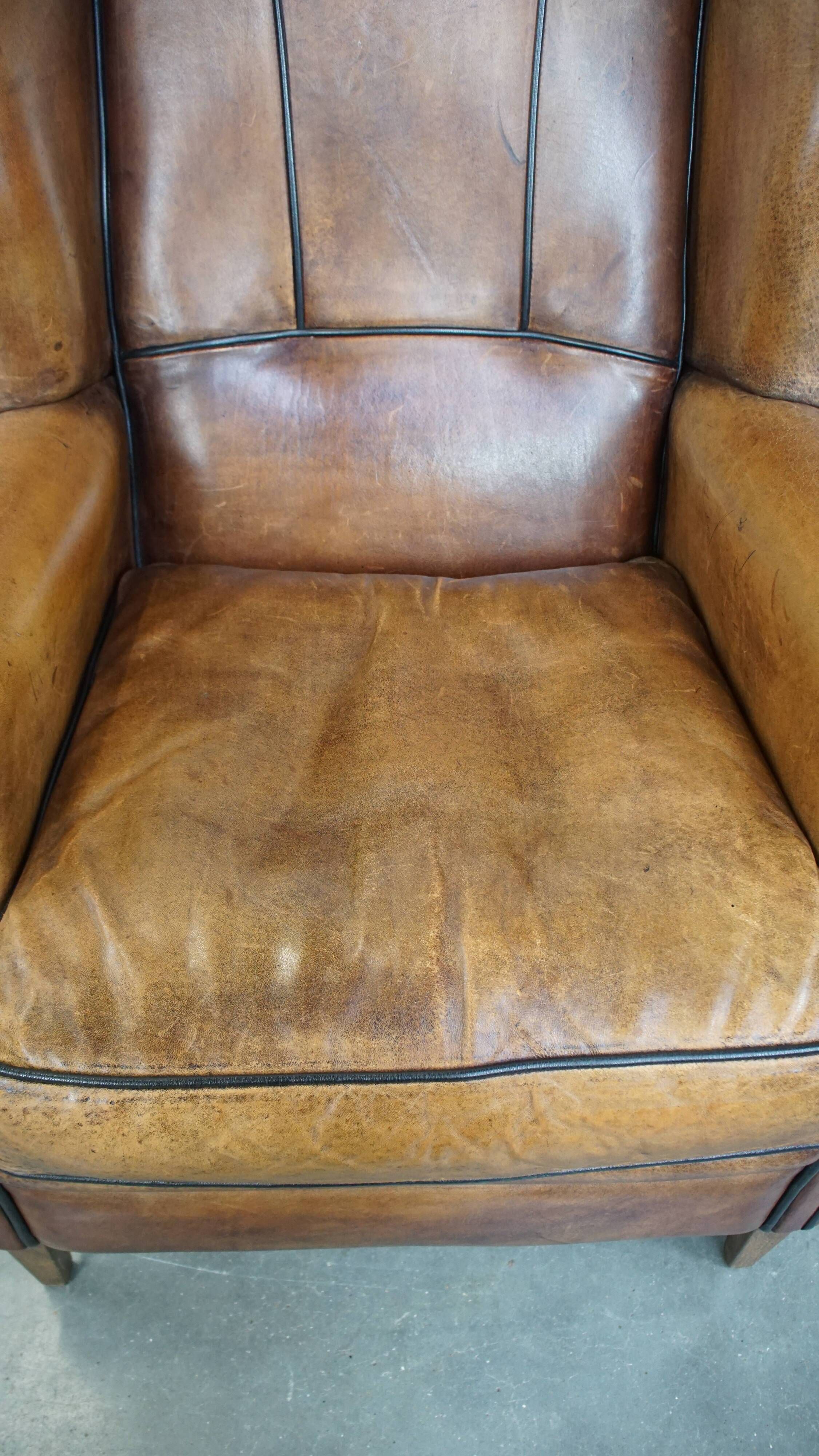 Cognac-colored sheep leather wingback chair finished with black piping